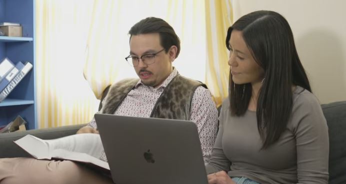 Un homme et une femme sont assis sur un canapé et consultent des documents sur un ordinateur portable et dans un livre de droit, à Iqaluit, au Nunavut, en juillet 2025.