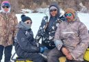 Quatre personnes, dont deux sur une motoneige, regardent en direction de l’appareil photo.