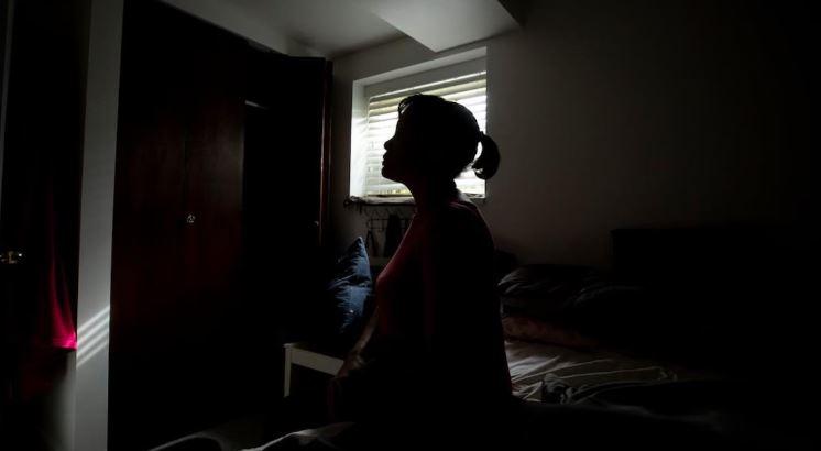 Une femme assise dans une chambre sombre.