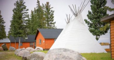 Un tipi entouré de chalets près d'un cours d'eau.