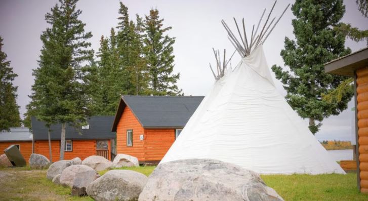 Un tipi entouré de chalets près d'un cours d'eau.