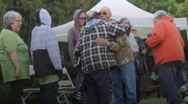 Un groupe de personnes se tient debout, parmi lesquelles deux hommes qui s’étreignent. 