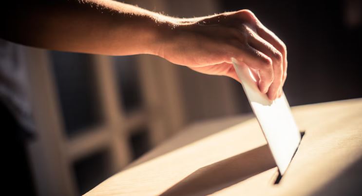 Gros plan sur une main qui dépose un bulletin de vote dans une boîte.