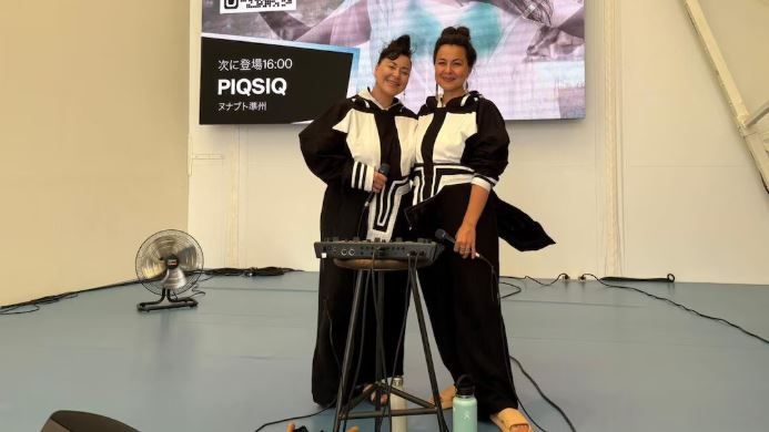 Les deux sœurs du duo PIQSIQ posent souriantes sur scène, vêtues de tenues noires et blanches d’inspiration traditionnelle.