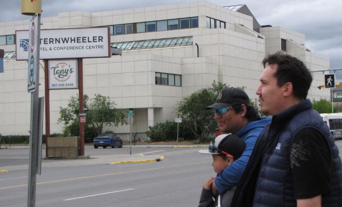 Deux hommes et un garçon attendent l'autobus au bord de la rue à Whitehorse.
