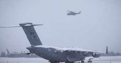 Un avion militaire canadien est à l’arrêt sur une piste enneigée tandis qu’un hélicoptère militaire vole au-dessus.