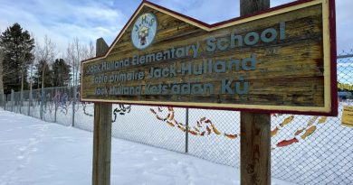 Le panneau de l'École primaire Jack Hulland à Whitehorse, au Yukon, devant une clôture décorée d'œuvres d'art.