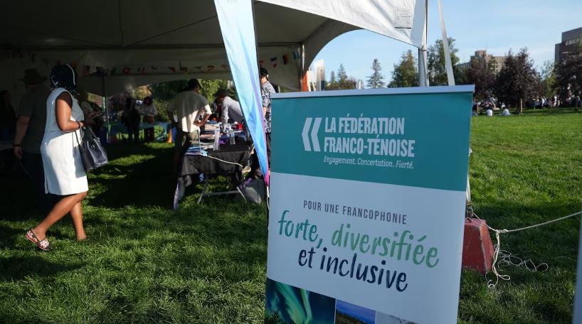 Un panneau de la Fédération franco-ténoise devant une tente abritant des exposants.