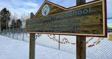Le panneau de l'École primaire Jack Hulland à Whitehorse, au Yukon, devant une clôture décorée d'œuvres d'art.