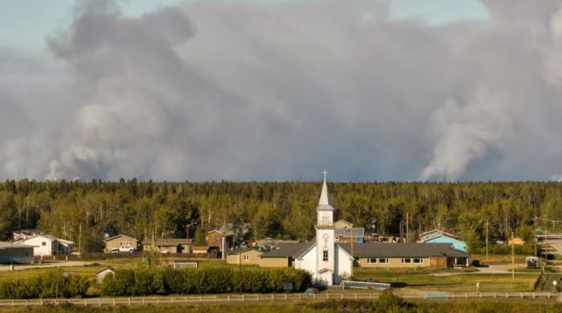 Une photo de Fort Providence avec de la fumée des feux de forêt en arrière-plan.