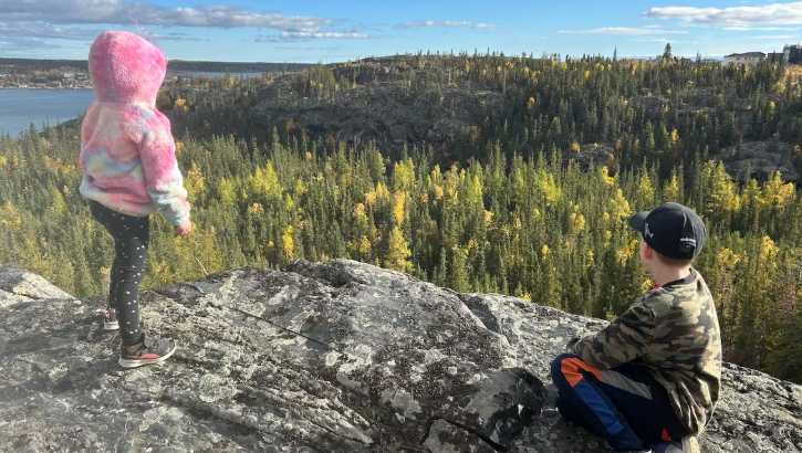 Deux enfants assis sur une roche en hauteur en train d'observer la nature.