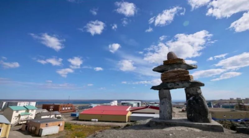 Un inukshuk en avant-plan avec le village de Rankin Inlet derrière.