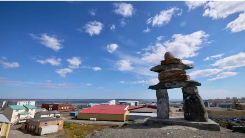 Un inukshuk en avant-plan avec le village de Rankin Inlet derrière.