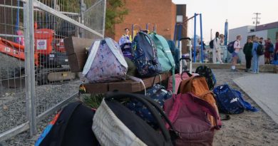 Des sacs à dos d'enfants entassés dans une cour d'école achalandée.