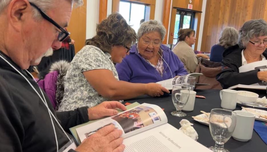 Des personnes assises à une table feuillettent un livre.