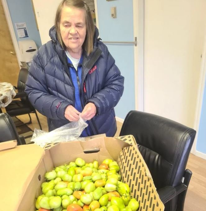 Celeste Goulet se tient à côté d'une boîte remplie de tomates vertes.