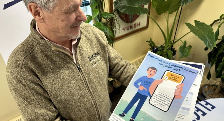 Le directeur général des élections, Maxwell Harvey, tient une affiche qui invite les citoyens à s'informer sur la réforme électorale auprès de son bureau.