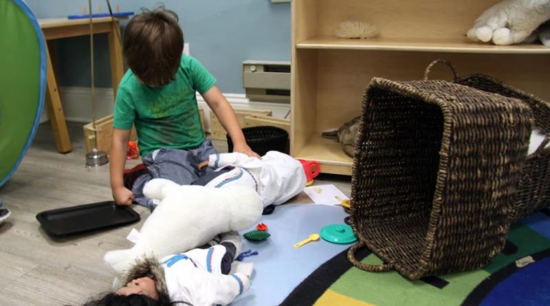 Enfant jouant avec un phoque et une poupée vêtue d'un amauti, un manteau traditionnel inuit.