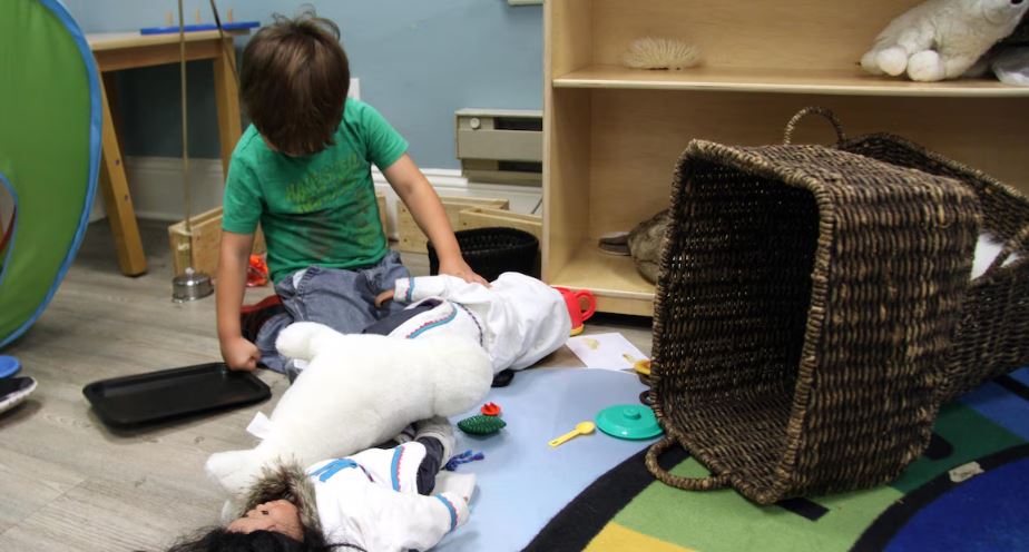 Enfant jouant avec un phoque et une poupée vêtue d'un amauti, un manteau traditionnel inuit.