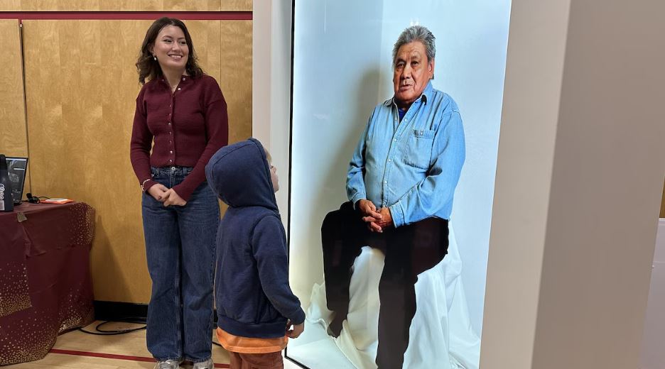 Un enfant regarde un grand écran qui montre l’image d’un homme assis.