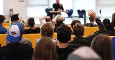 Photo du forum communautaire avec des élèves en premier plan et un candidat en arrière-plan.