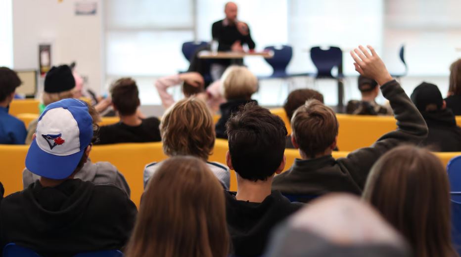Photo du forum communautaire avec des élèves en premier plan et un candidat en arrière-plan.