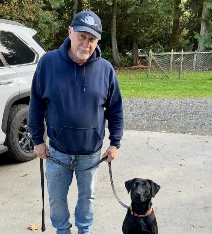 Un homme tient en laisse un chien noir.