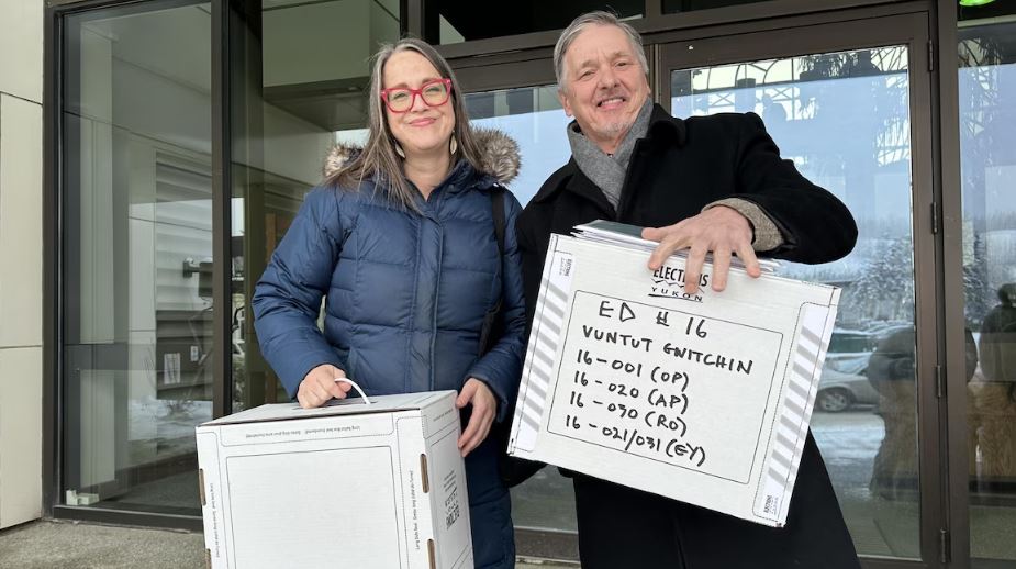 La directrice du scrutin dans Vuntut Gwitchin et le directeur général des élections se tiennent devant le palais de justice avec les boîtes ayant servi au dépouillement judiciaire.