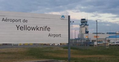 Une pancarte affichant l'aéroport de Yellowknife, avec en arrière-plan la tour de contrôle.