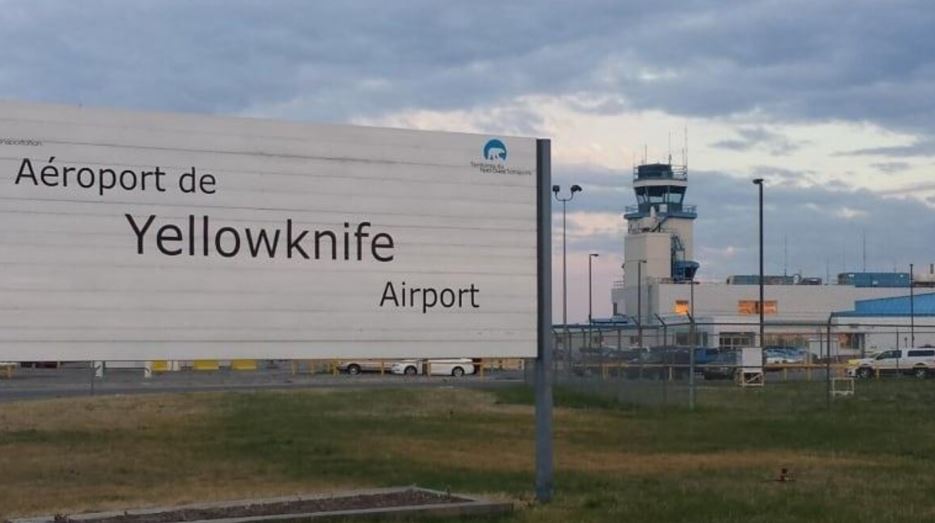 Une pancarte affichant l'aéroport de Yellowknife, avec en arrière-plan la tour de contrôle.