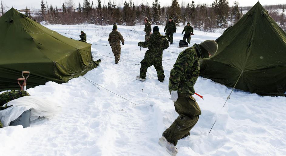 Des militaires vêtus de tenues de camouflage vertes posent des tentes dans la neige lors de l'opération Nanook, à Inuvik, aux Territoires du Nord-Ouest, le 2 mars 2025.