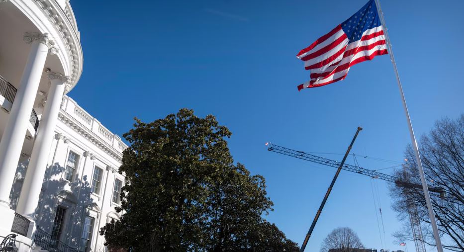 Une grue s'élève à côté de la Maison-Blanche et un drapeau américain est hissé.