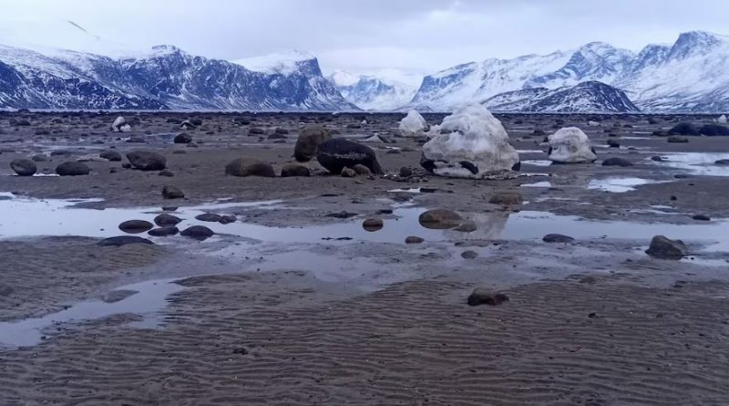 Un rivage parsemé de flaques d'eau et des montagnes au loin.