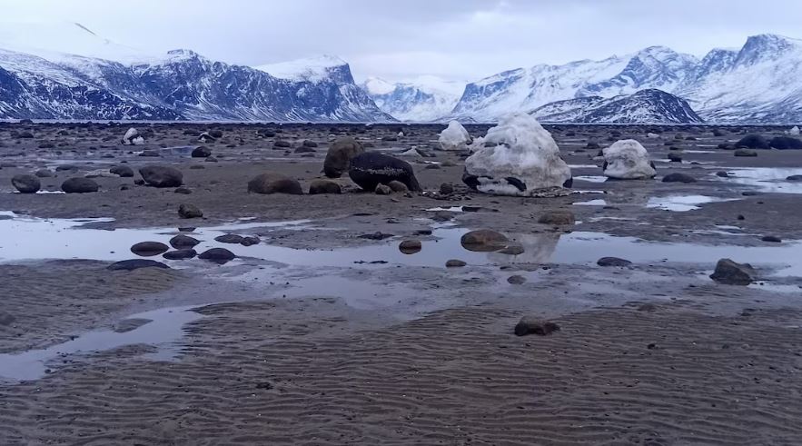 Un rivage parsemé de flaques d'eau et des montagnes au loin.