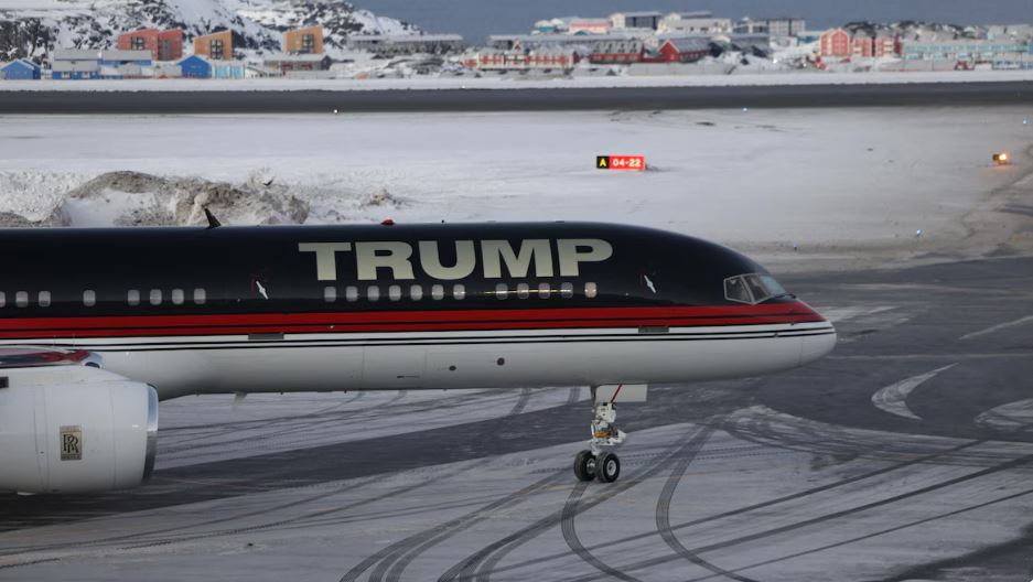 Un avion sur lequel est écrit « Trump » est posé devant un paysage de neige et de maisons.