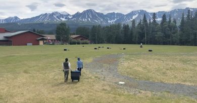 Deux personnes transportent un bac sur un terrain à Haines Junction contenant des instruments scientifiques pour mesurer le risque sismique.