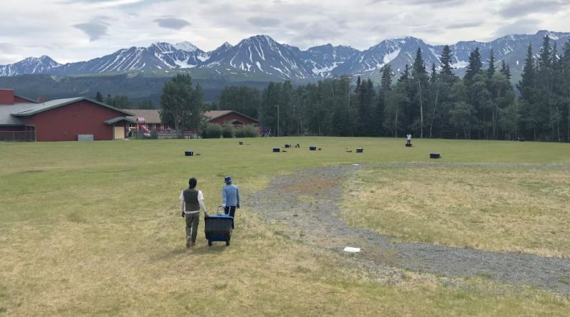 Deux personnes transportent un bac sur un terrain à Haines Junction contenant des instruments scientifiques pour mesurer le risque sismique.