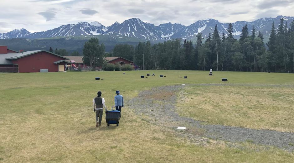 Deux personnes transportent un bac sur un terrain à Haines Junction contenant des instruments scientifiques pour mesurer le risque sismique.