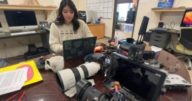Une femme travaille sur un ordinateur portable posé sur une table couverte d'appareils électroniques et d'appareils photo.