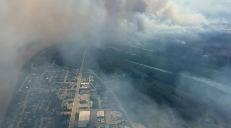 Une vue aérienne de Fort Simpson montrant des colonnes de fumée s’élevant de la forêt environnantes.