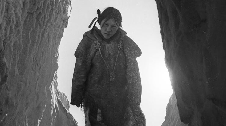 Une photo d'archives en noir et blanc avec une adolescente dans l'encadrement d'une porte, les pieds sur des marches faites de neige.