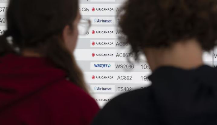 Deux femmes, de dos, regardent une liste de vols sur un écran.